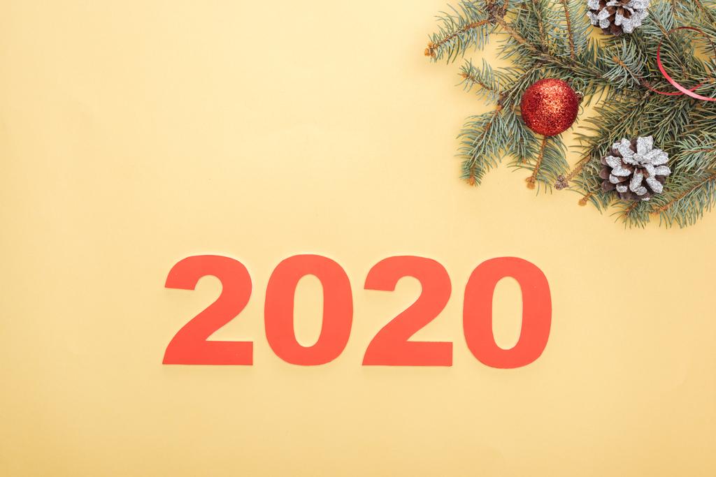 Draufsicht auf Papier 2020 Zahlen in der Nähe von Weihnachtsbaum Zweig mit Kugeln und Zapfen auf gelbem Hintergrund - Foto, Bild