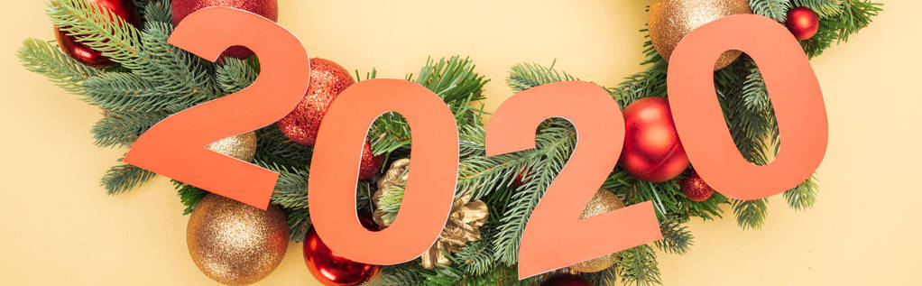 bovenaanzicht van papier 2020 nummers nabij kerstboom tak met kerstballen op gele achtergrond - Foto, afbeelding