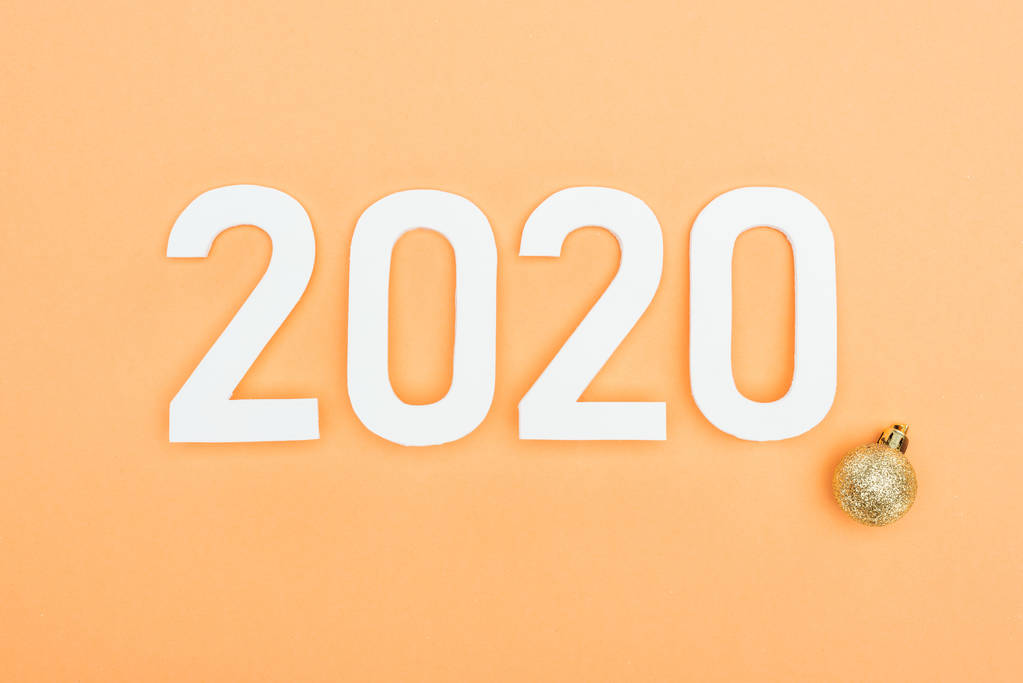 bovenaanzicht van witte 2020 nummers bij gouden kerstbal op oranje achtergrond - Foto, afbeelding