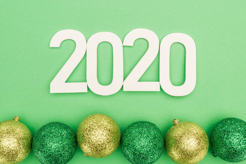 緑の背景にあるクリスマス・バブルの近くの白い2020年の数字のトップビュー - 写真・画像