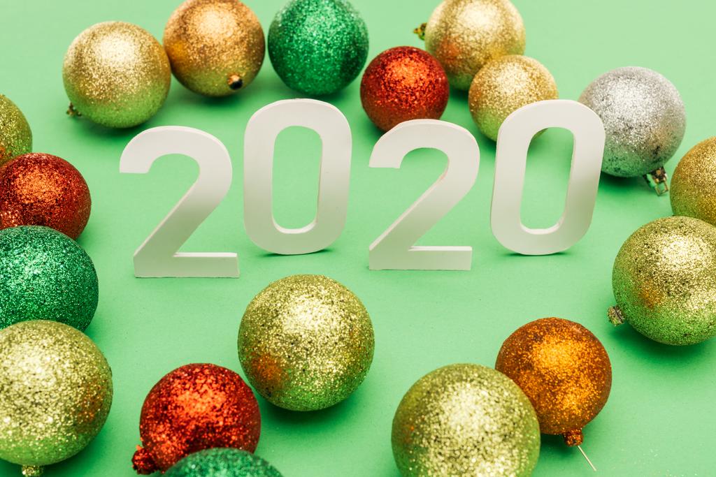 números blancos 2020 cerca de bolas de Navidad multicolores sobre fondo verde
 - Foto, imagen