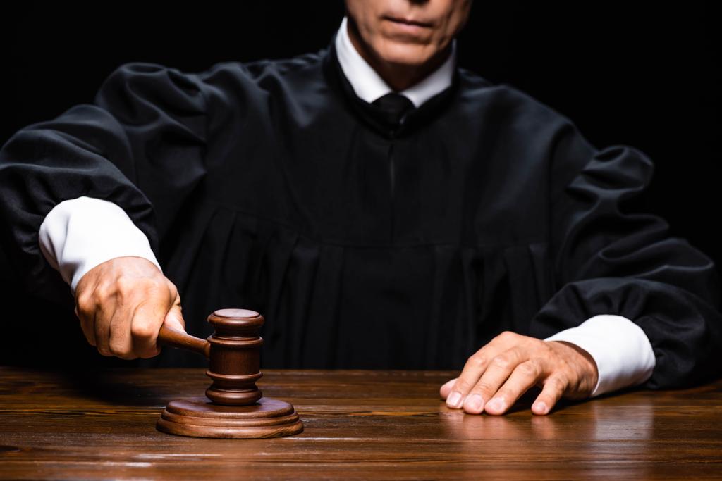 обрізаний вид на суддю в судовому халаті, сидячи за столом і вдарившись з подарунком ізольовано на чорному
 - Фото, зображення