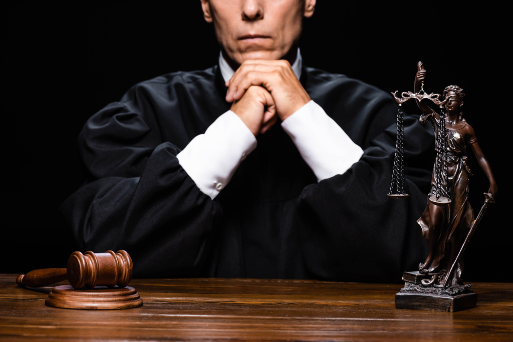 levágott kilátás bíró bíróság köntösben ül asztalnál kalapáccsal és themis figura elszigetelt fekete - Fotó, kép