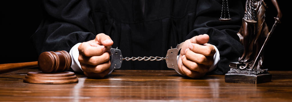 панорамний знімок судді в судовому халаті, сидячи за столом з наручниками ізольовані на чорному
 - Фото, зображення