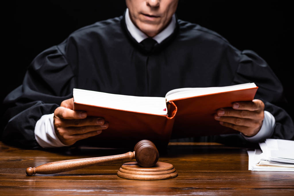Yargı bornozu giymiş yargıcın masada oturup siyah üzerine izole edilmiş turuncu kitap okuması. - Fotoğraf, Görsel
