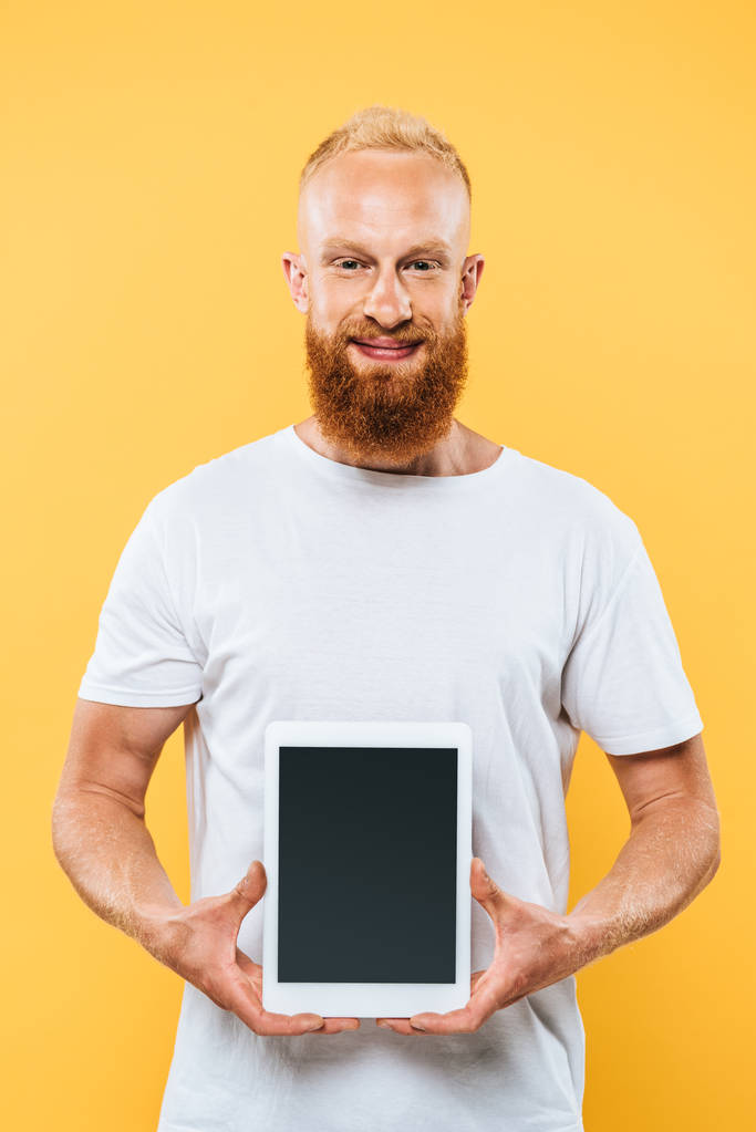 mosolygó szakállas férfi mutatja digitális tabletta üres képernyőn, elszigetelt sárga - Fotó, kép
