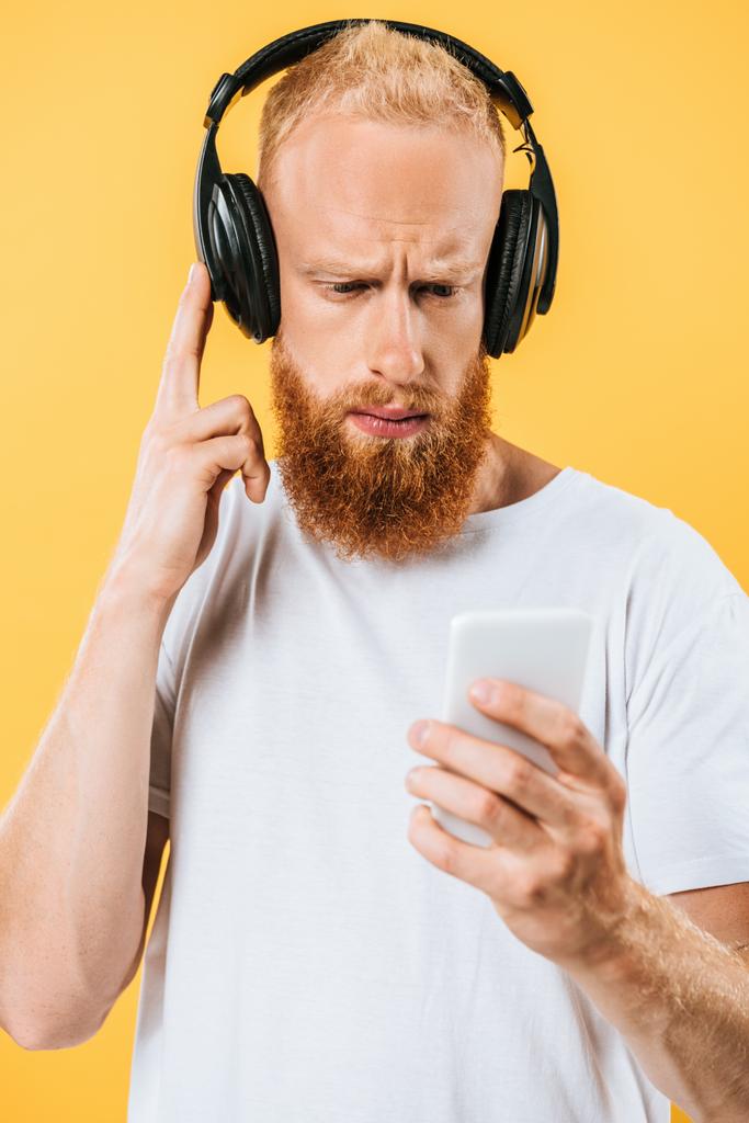 thoughtful beard man listening music with headphones and smartphone, isolated on yellow - Photo, Image