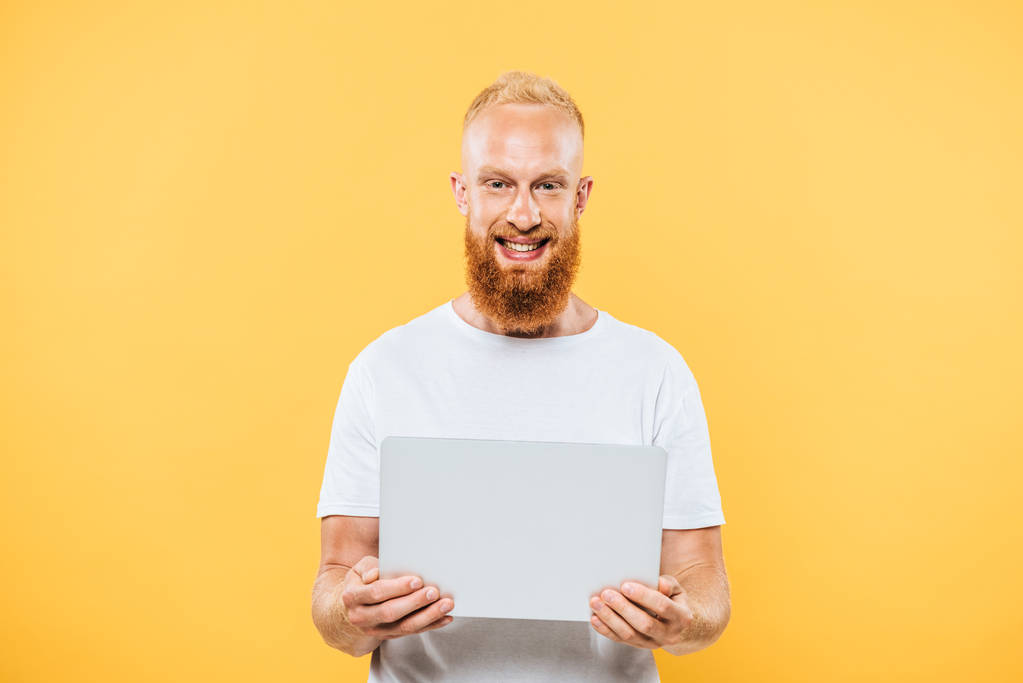 幸せな髭を生やした男がノートパソコンを使って黄色に隔離され - 写真・画像