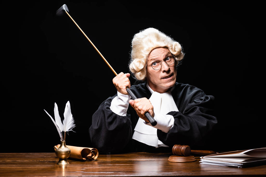 θυμωμένος δικαστής με δικαστικό χιτώνα και περούκα κρατώντας μπαστούνι του γκολφ απομονωμένο σε μαύρο - Φωτογραφία, εικόνα