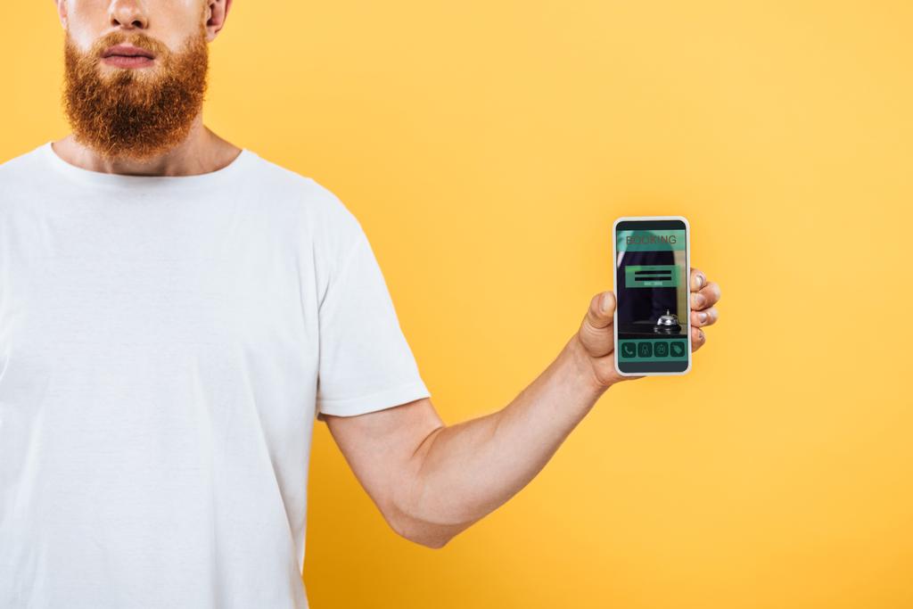 rajattu näkymä parrakas mies osoittaa älypuhelin varaus app, eristetty keltainen
 - Valokuva, kuva