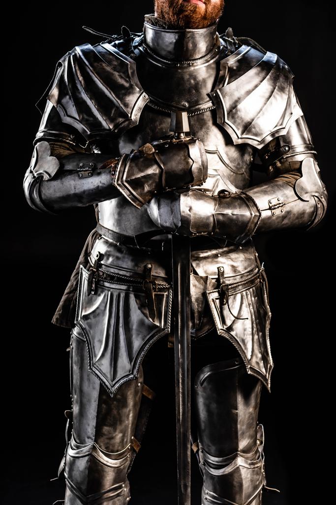 обрезанный вид рыцаря в доспехах, держащего меч изолированный на черном
  - Фото, изображение