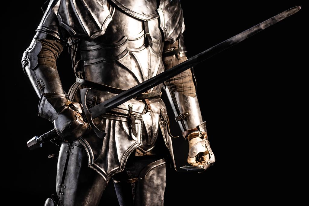 обрізаний вид на лицаря в обладунках, що тримає меч ізольовано на чорному
  - Фото, зображення