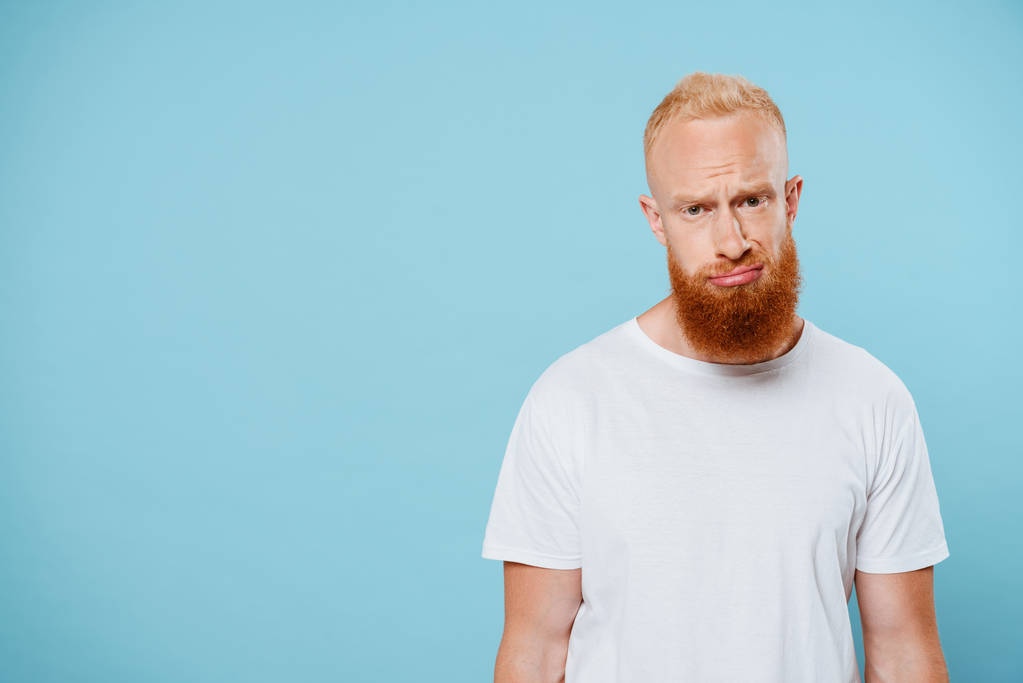 портрет расстроенного бородатого мужчины в белой футболке, изолированный на голубом
  - Фото, изображение