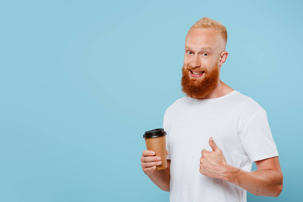 bärtiger Mann im T-Shirt, Daumen hoch mit Coffee to go, isoliert auf blauem Grund - Foto, Bild