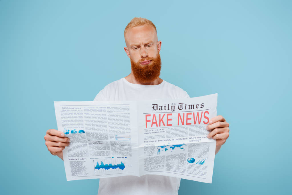 skeptical bearded man reading newspaper with fake news, isolated on blue - Photo, Image