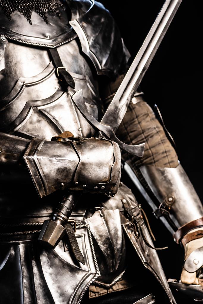 vista recortada de caballero en la armadura que sostiene la espada aislado en negro
  - Foto, imagen