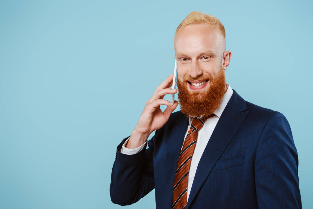 sonriente hombre de negocios barbudo hablando en el teléfono inteligente, aislado en azul
 - Foto, imagen