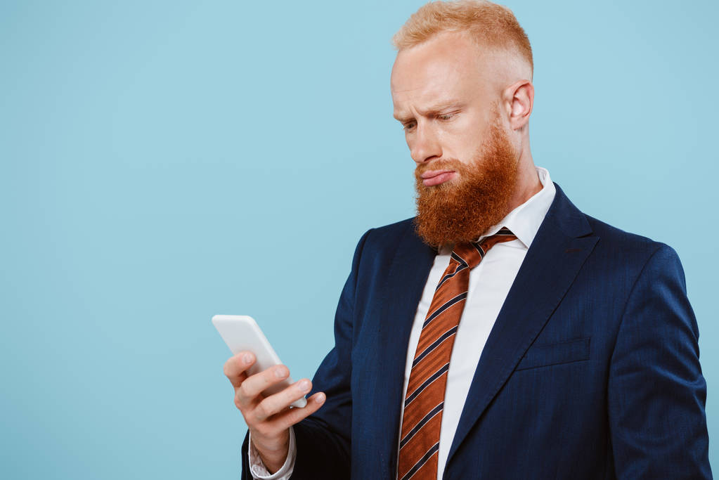hombre de negocios barbudo confundido hablando en el teléfono inteligente, aislado en azul
 - Foto, imagen