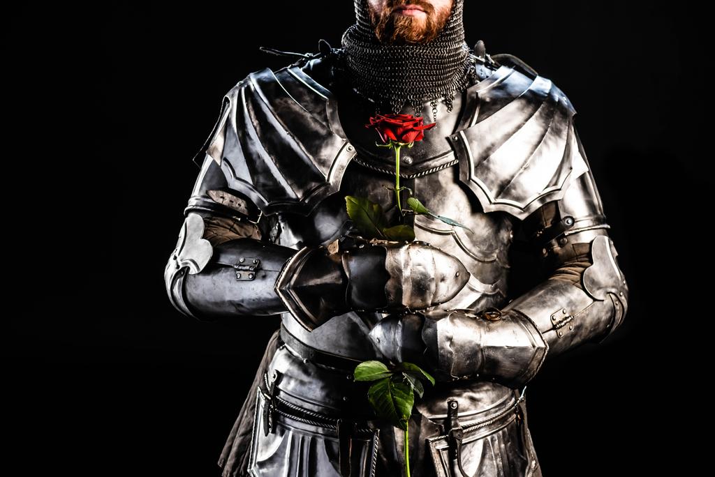 oříznutý pohled na rytíře v brnění držícího růži izolovanou na černém  - Fotografie, Obrázek
