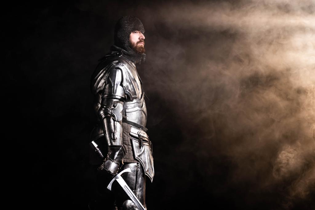 Siyah arka planda kılıç tutan zırhlı yakışıklı bir şövalye. - Fotoğraf, Görsel