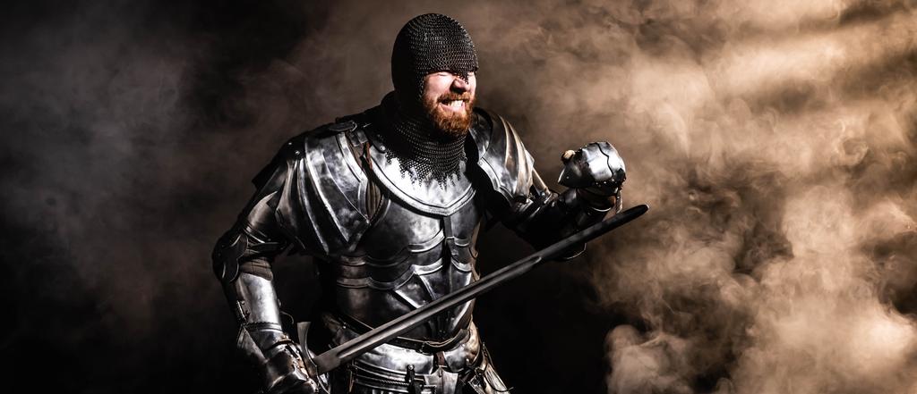 tiro panorâmico de belo cavaleiro em armadura segurando espada e lutando no fundo preto
 - Foto, Imagem