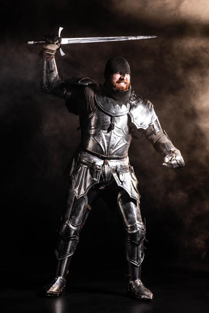 pohledný rytíř v brnění drží meč a boj na černém pozadí - Fotografie, Obrázek