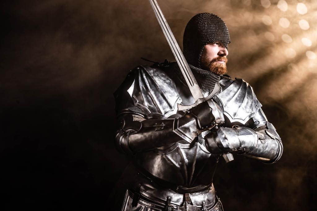 handsome knight in armor holding sword on black background - Photo, Image