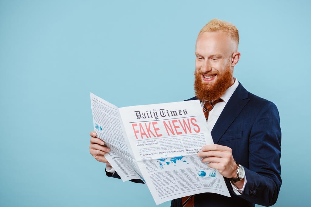cheerful bearded businessman reading newspaper with fake news, isolated on blue - Photo, Image