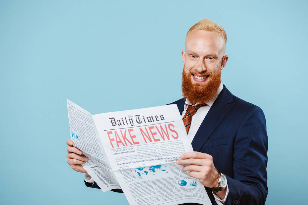 Улыбающийся бородатый бизнесмен читает газету с фальшивыми новостями, изолированными на голубом
 - Фото, изображение