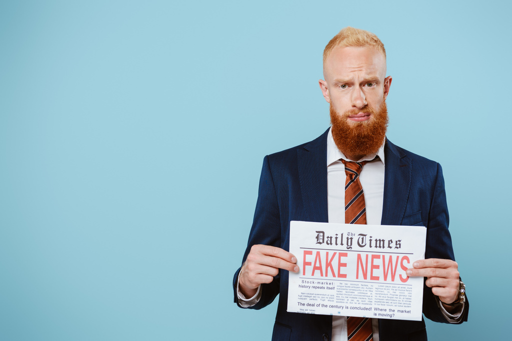 тривожний бородатий бізнесмен тримає газету з фальшивими новинами, ізольовані на синьому
 - Фото, зображення