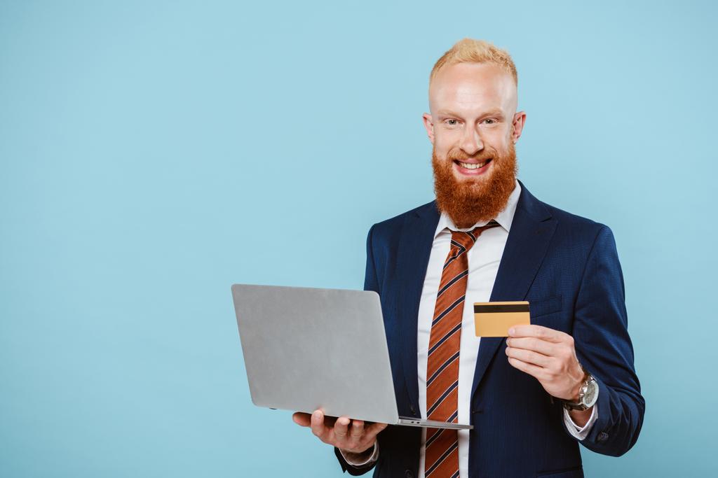 счастливый бородатый бизнесмен в костюме покупки онлайн с кредитной картой и ноутбуком, изолированные на синий
 - Фото, изображение