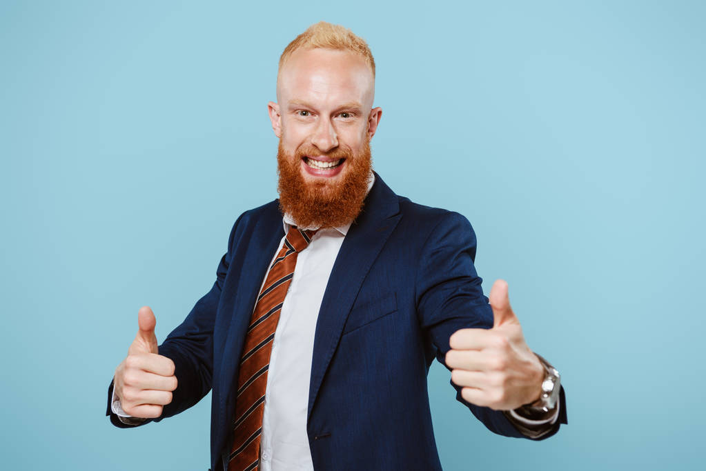 izgatott szakállas üzletember öltönyben mutatja hüvelykujját felfelé, elszigetelt kék - Fotó, kép