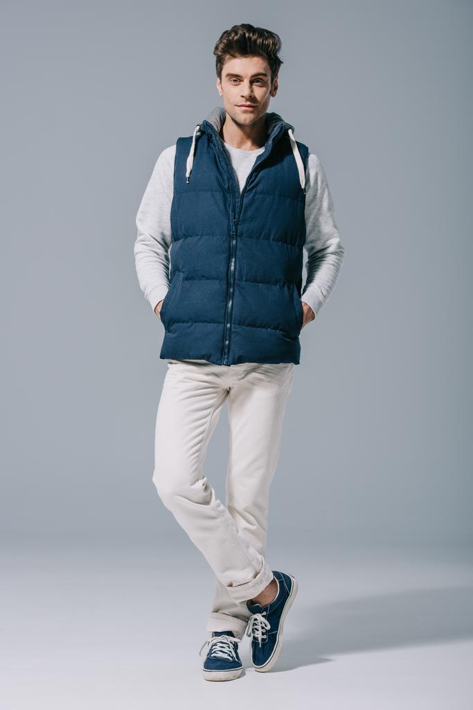 pohledný módní muž pózující ve vestě na šedé - Fotografie, Obrázek