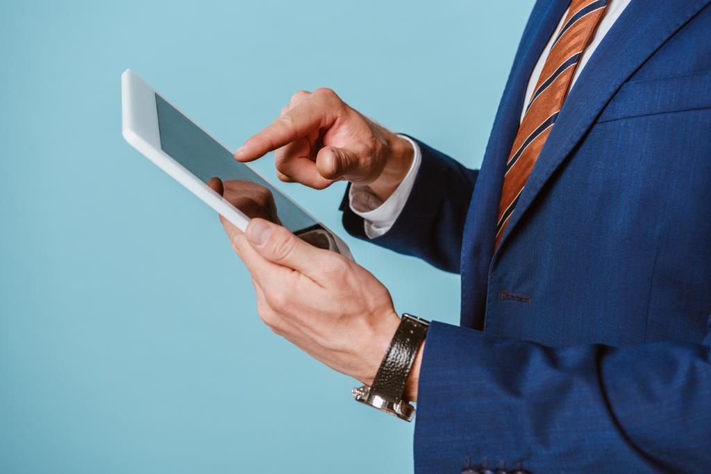 bijgesneden beeld van zakenman in pak met behulp van digitale tablet, geïsoleerd op blauw - Foto, afbeelding