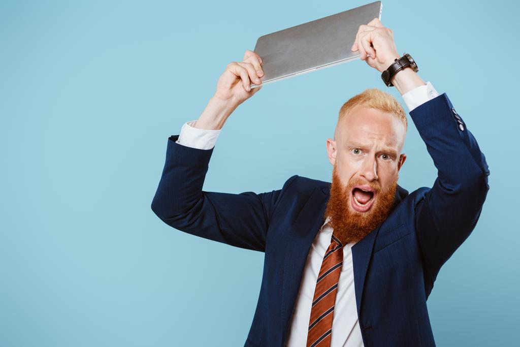 agresszív szakállas üzletember kiabál és laptopot dobál, elszigetelt kék - Fotó, kép