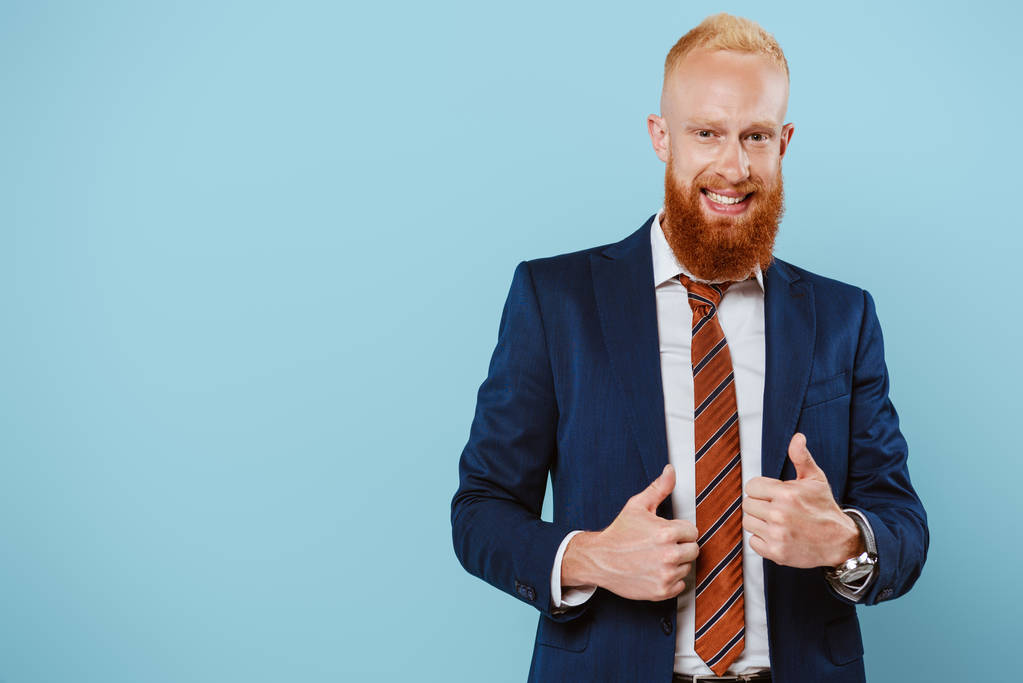handsome bearded businessman in suit showing thumbs up, isolated on blue - Photo, Image