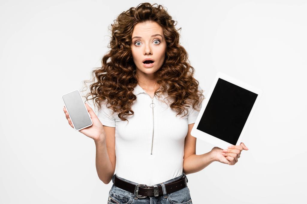 Schockierte Frau zeigt Smartphone und digitales Tablet, isoliert auf weiß - Foto, Bild
