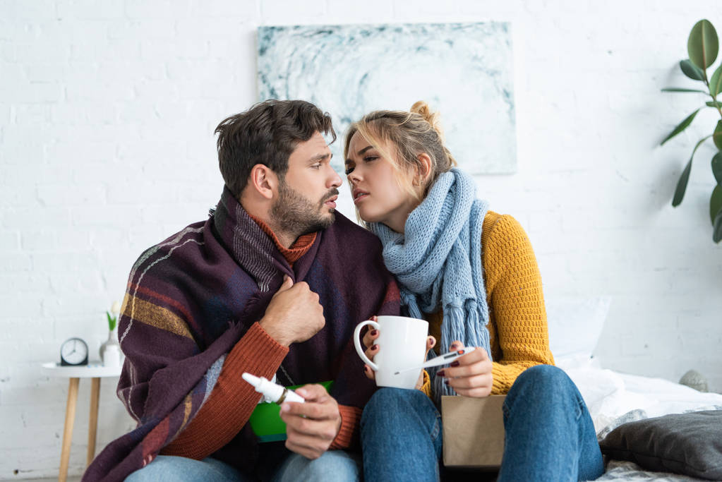 Erkranktes Paar hält Thermometer, Heißgetränk und Nasenspray im Schlafzimmer - Foto, Bild