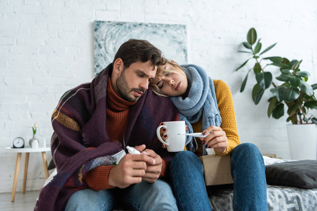 ill couple holding thermometer, hot drink and nasal spray in bedroom - Photo, Image