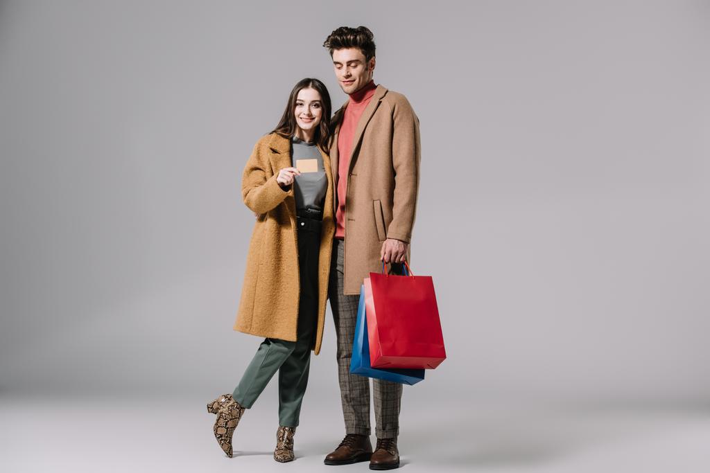 gyönyörű pár bézs kabát pózol bevásárló táskák és hitelkártya szürke - Fotó, kép