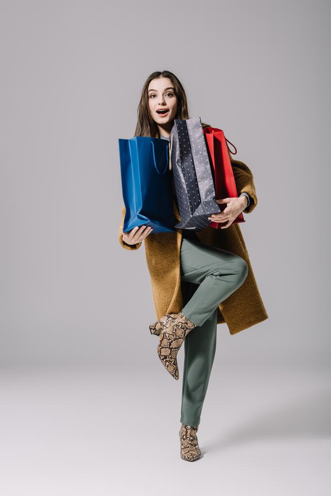 divatos meglepett nő bézs kabátban kezében bevásárló táskák szürke - Fotó, kép