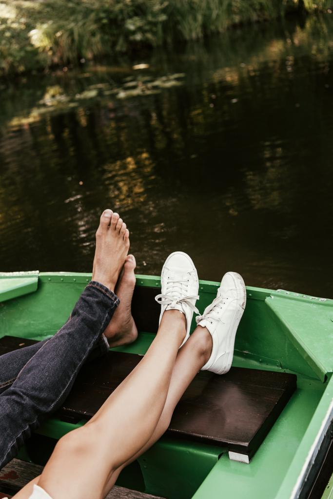 cropped view of barefoot man and girl in sneakers relaxing in boat on lake - Photo, Image