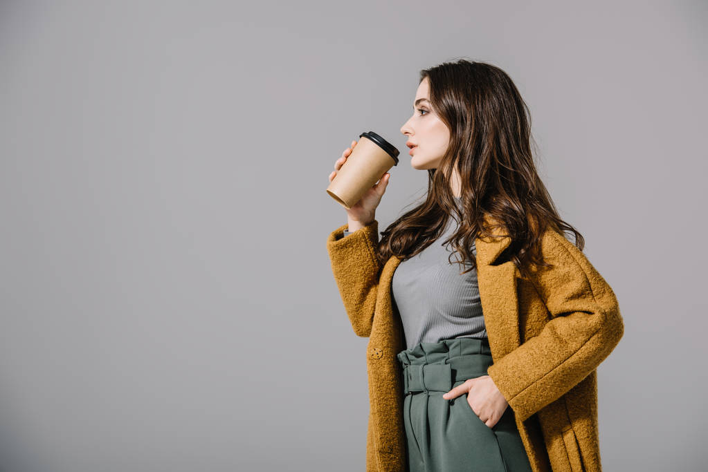 schöne Frau im beigen Mantel, die Coffee to go trinkt, isoliert auf grau  - Foto, Bild