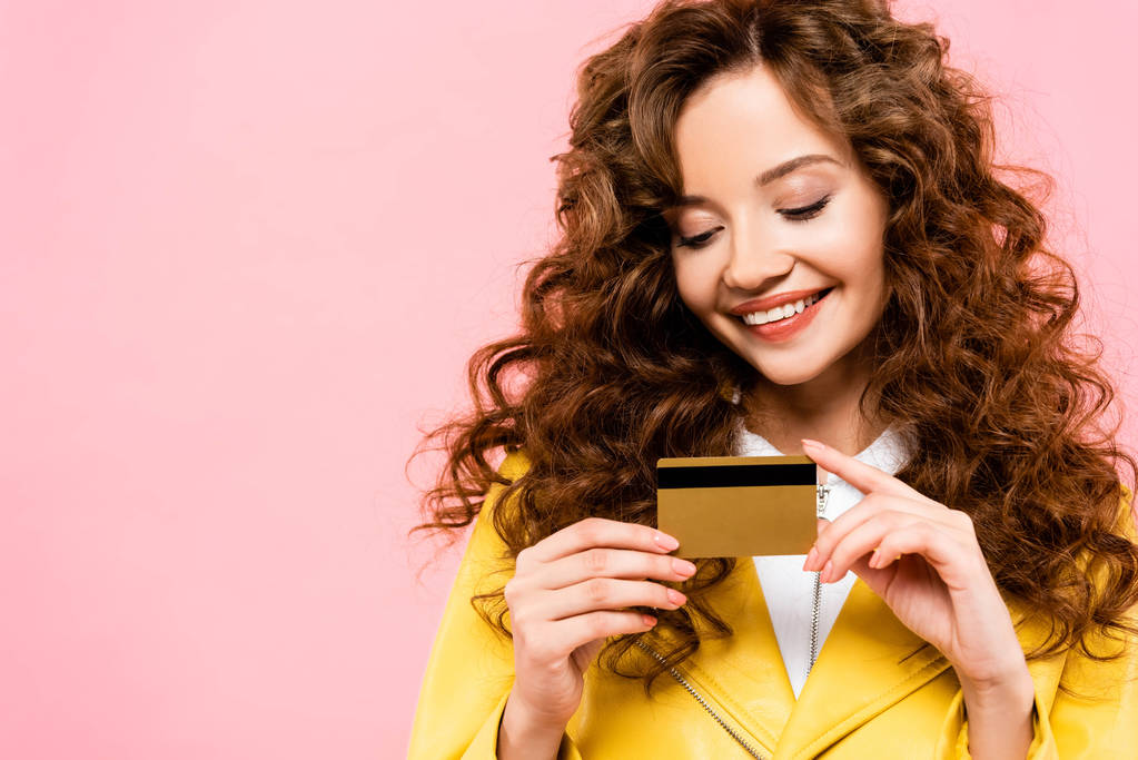smiling curly girl holding credit card, isolated on pink - Photo, Image