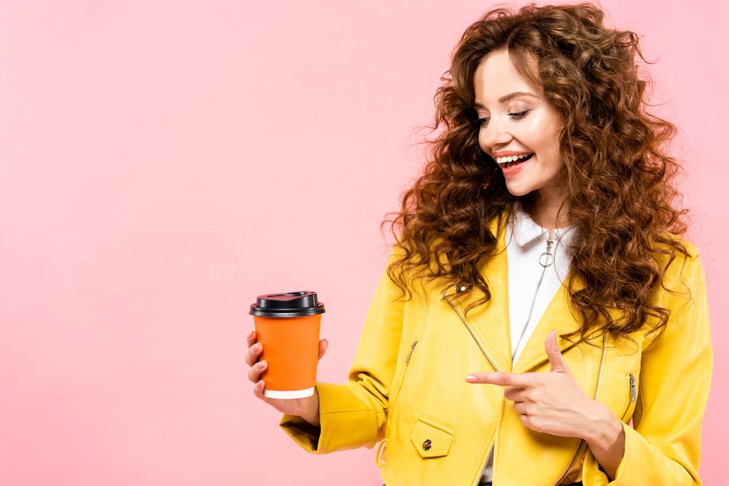 piękna uśmiechnięta kobieta wskazująca na kawę na wynos, odizolowana na różowo - Zdjęcie, obraz