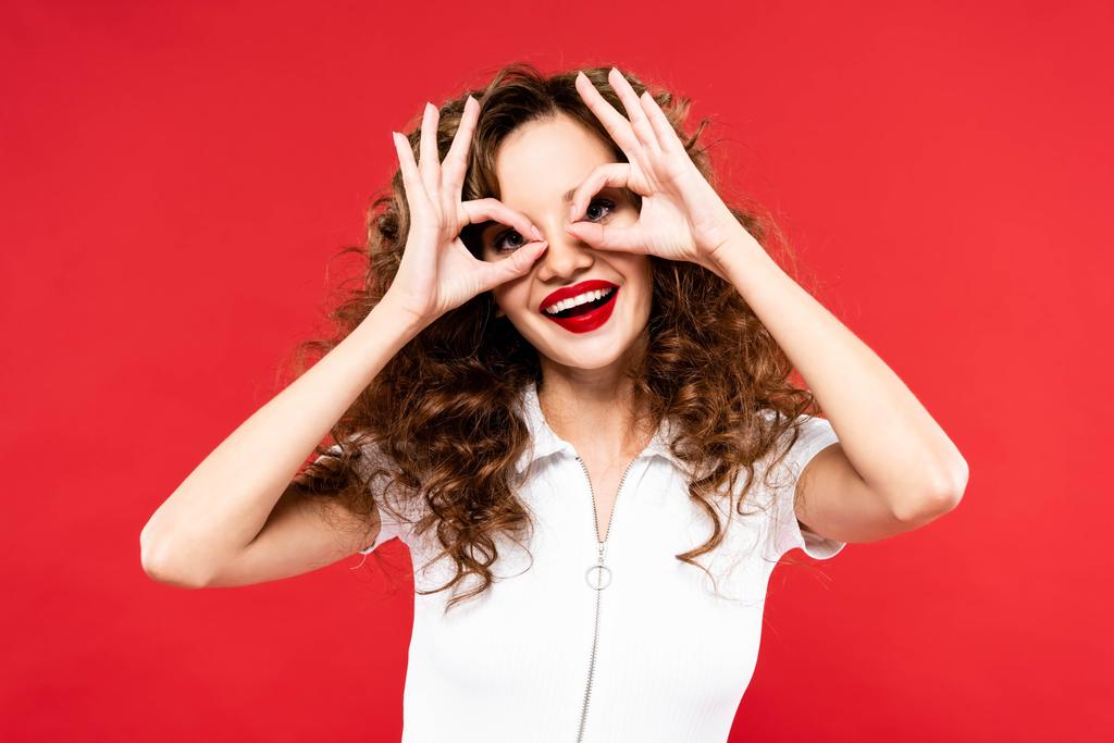 divertida chica rizada haciendo gafas de las manos, aislado en rojo
 - Foto, imagen