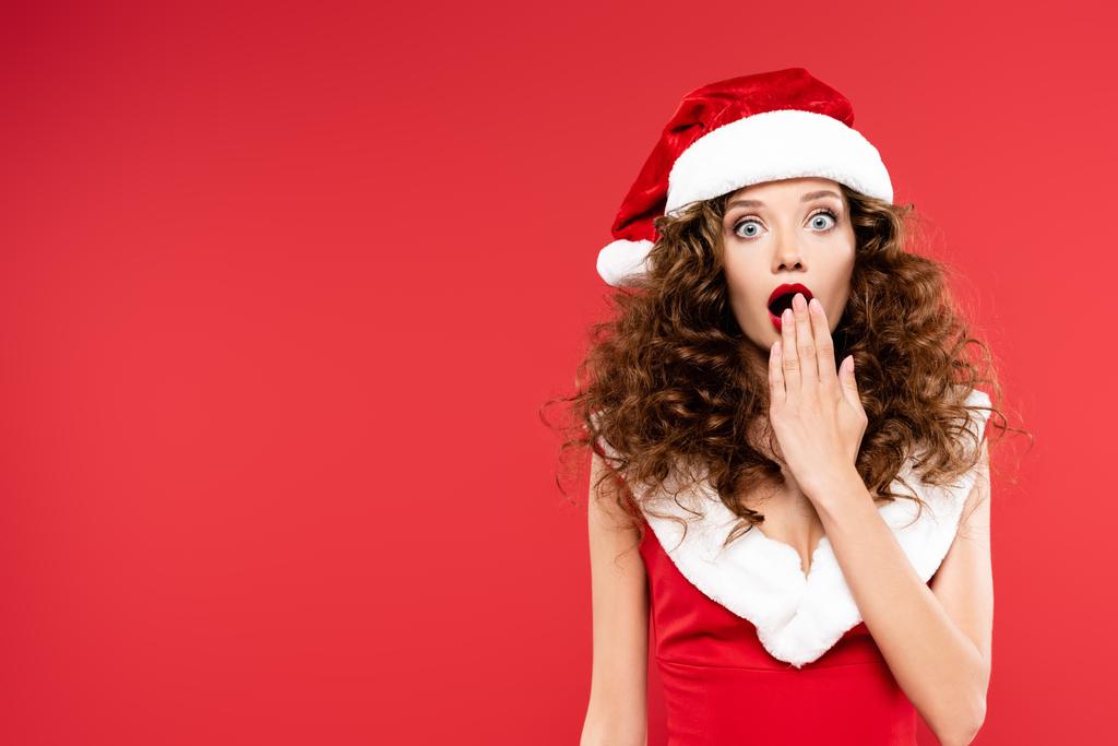 happy surprised girl gesturing in santa costume, isolated on red - Photo, Image