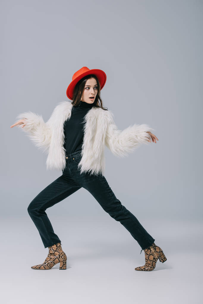 chica elegante de moda posando en abrigo de piel blanca y sombrero rojo en gris
 - Foto, Imagen