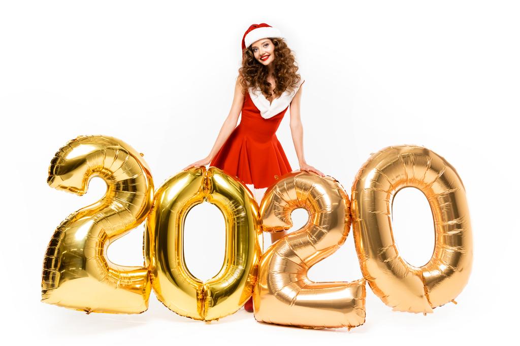 chica atractiva en traje de santa posando con globos de oro 2020 año nuevo, aislado en blanco
 - Foto, imagen