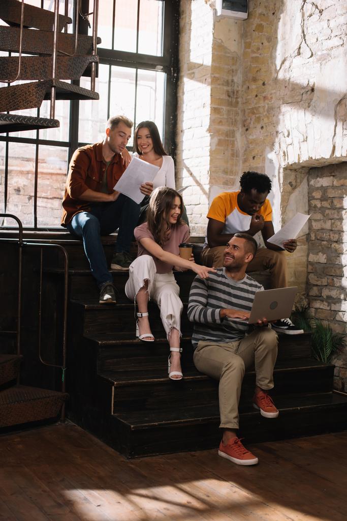veselí, mladí multikulturní podnikatelé mluví, zatímco sedí na schodech - Fotografie, Obrázek